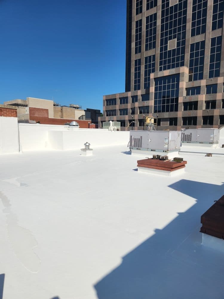 White flat commercial roof with HVAC units and city skyline in background on sunny day.