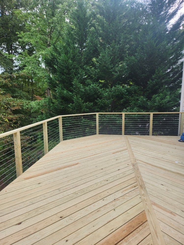 Wooden deck with wire railing surrounded by lush green trees in a serene outdoor setting.