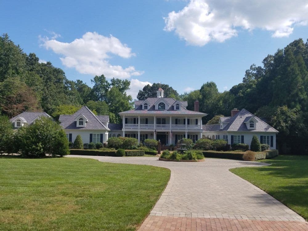 Spacious luxury home with landscaped gardens and a paved driveway against a blue sky.