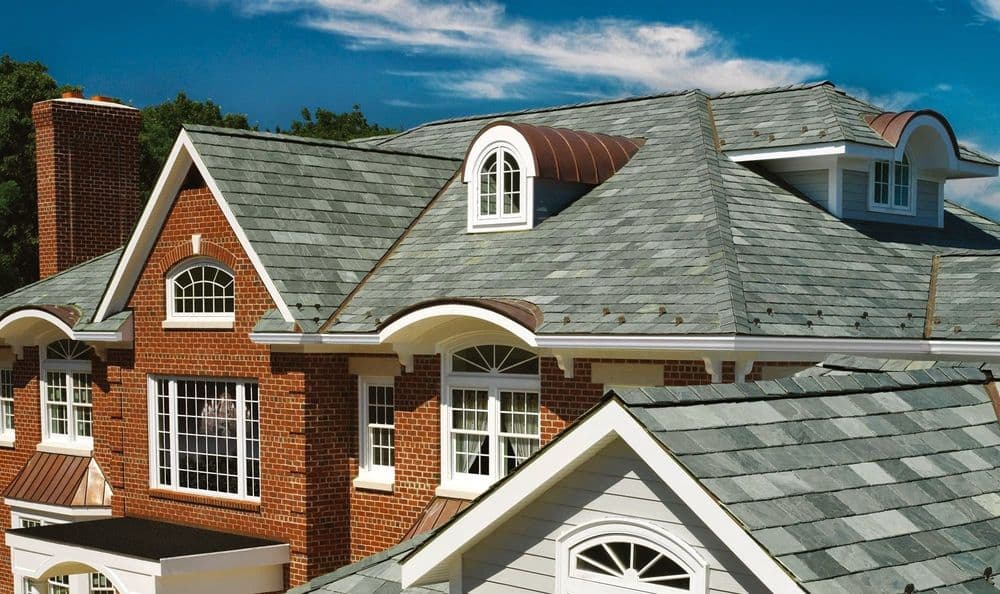 Elegant slate roof on a modern brick house with multiple gables and windows. Blue sky backdrop.