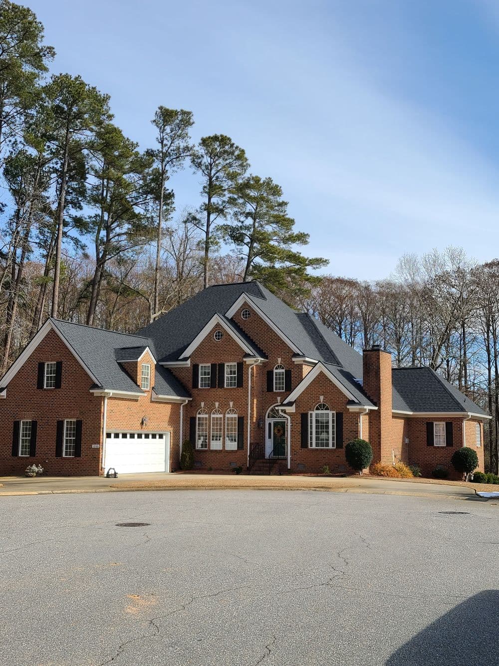 Brick house with a large front yard and garage, surrounded by tall trees on a quiet street.